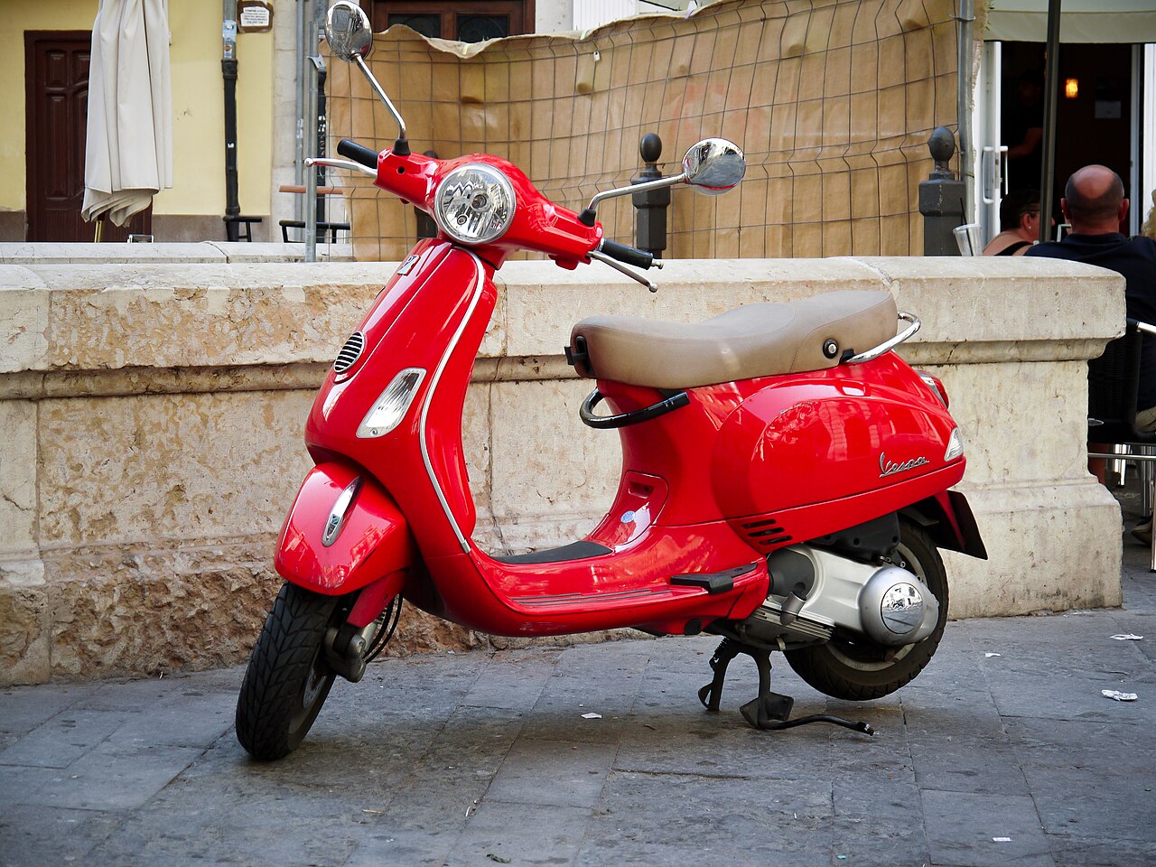 Real red Vespa motor scooter parked by a stone wall, illustrating a classic motor scooter