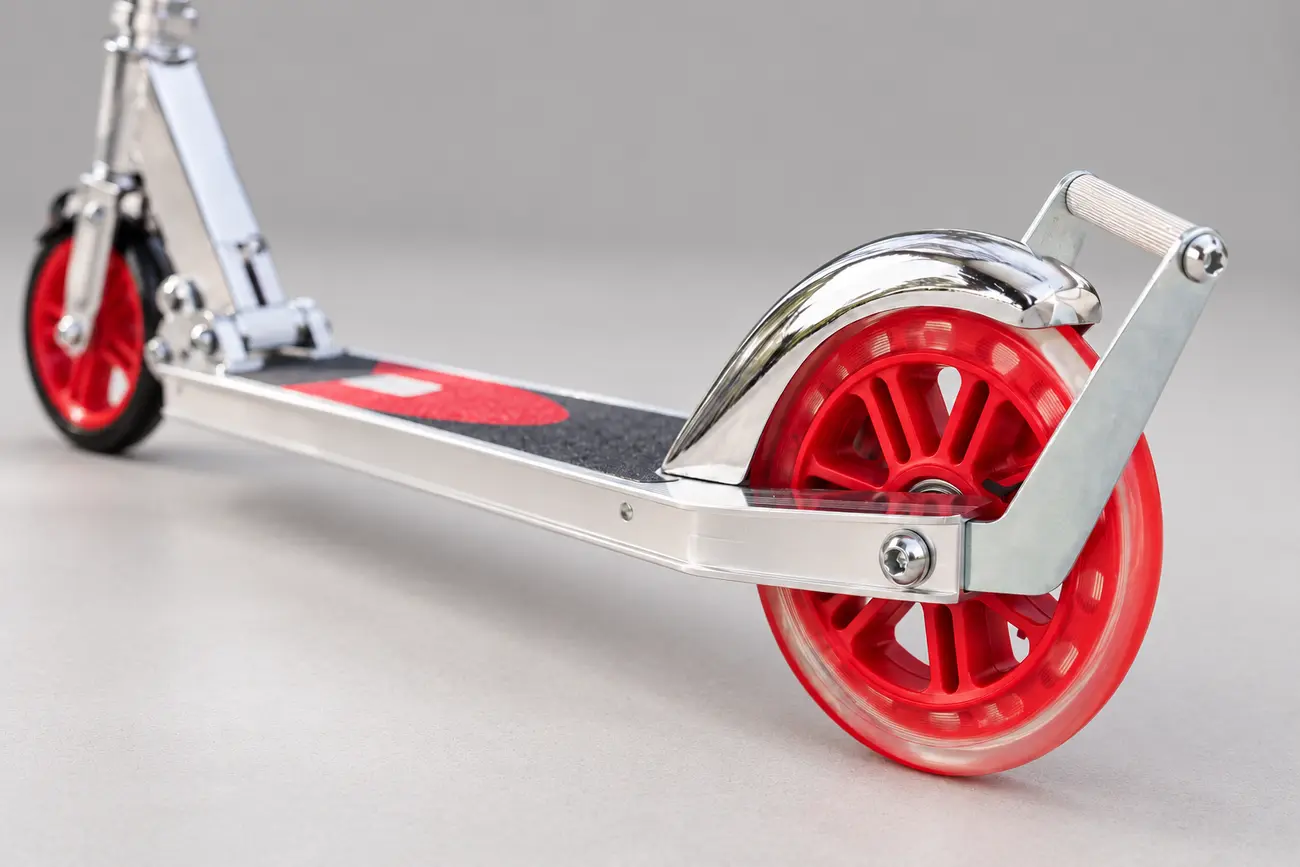 Close-up illustration of the red eight-inch rear wheel and curved metal rear-fender foot brake on a Razor A5 Lux manual kick scooter against a plain gray studio background